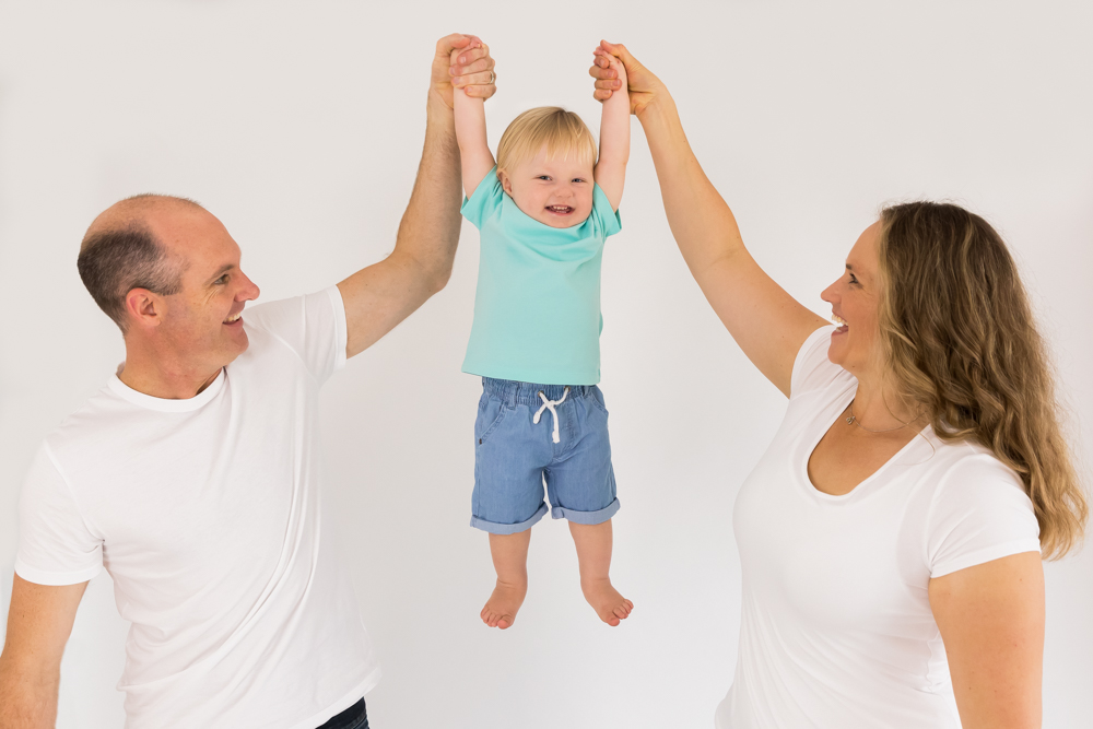 Fun family portrait with Mum and dad lifting up toddler