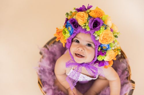smiling baby girl sitting in colourful bonnet studio portrait