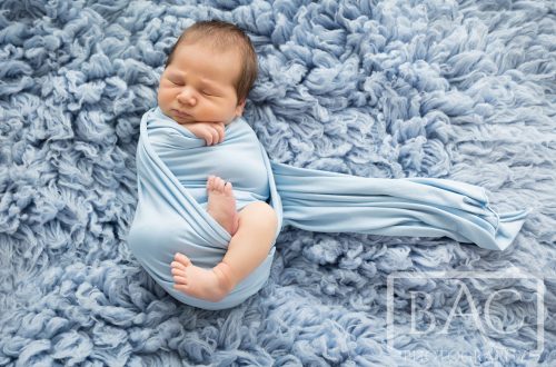 chubby swaddled newborn on blue rug