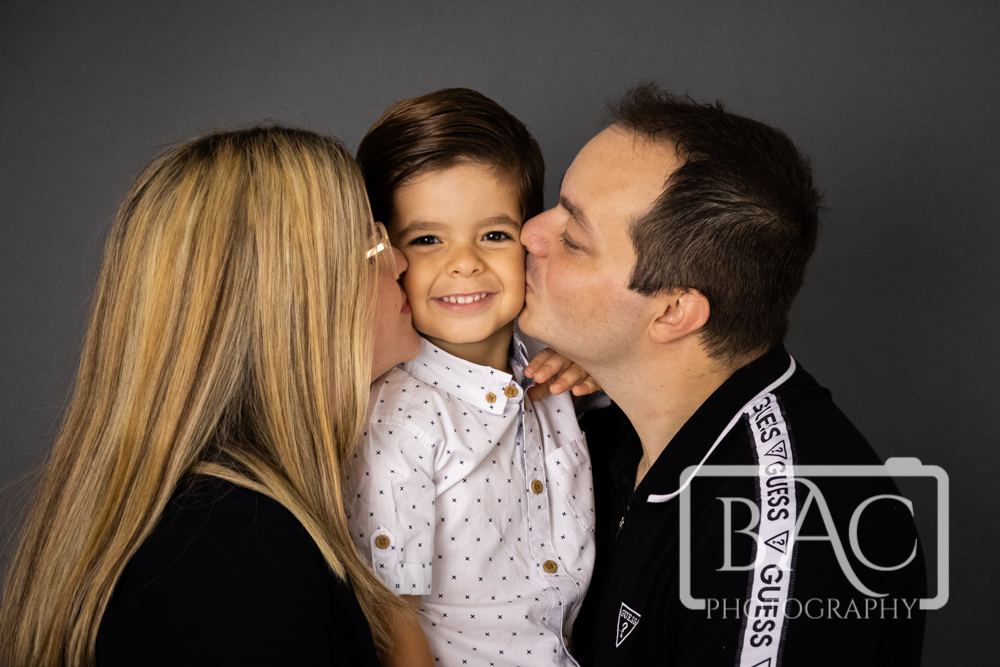 kisses for a little boy mum dad and son studio portrait